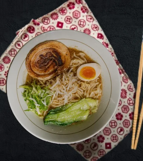 A top-down view of tonkotsu ramen with grilled pork belly, soft egg and greens